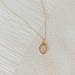 Gold necklace with a locket pendant on a textured beige surface