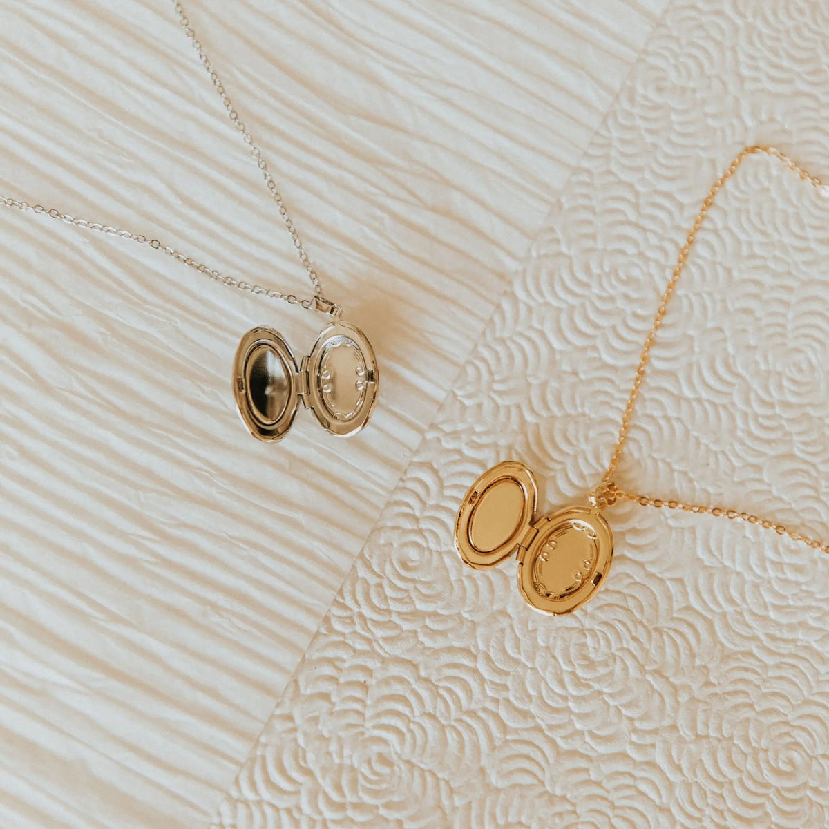 Two gold necklaces with lockets on a textured beige background