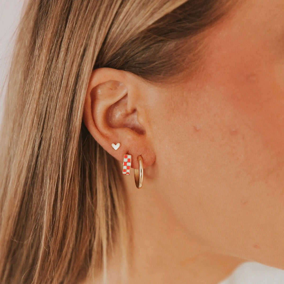 Close-up of an ear wearing a gold hoop earring with a small heart-shaped stud.