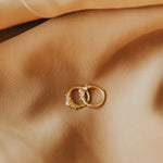 Pair of gold hoop earrings with small pearls on a beige fabric background