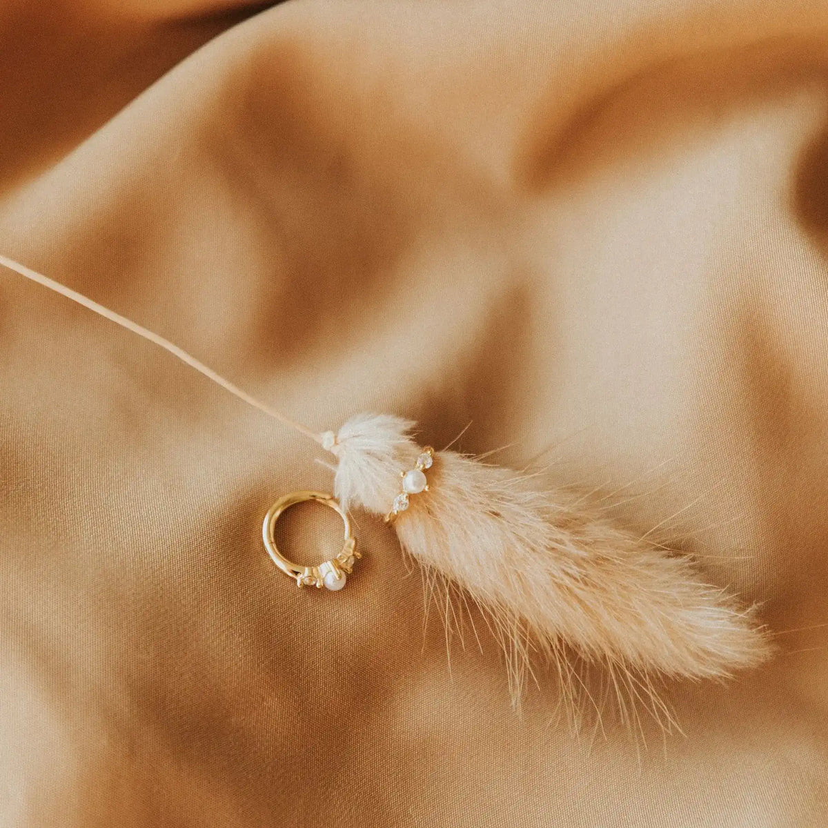 Gold earing with pearls and a feather on a beige fabric background