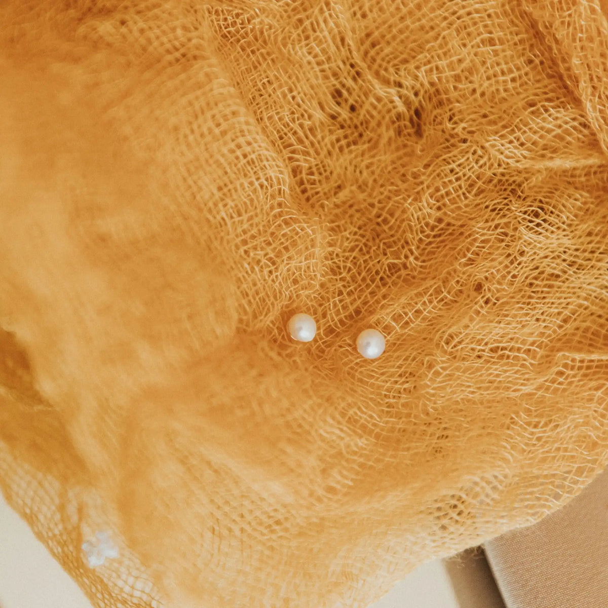 Close-up of a yellow cloth with two small pearl earrings on top