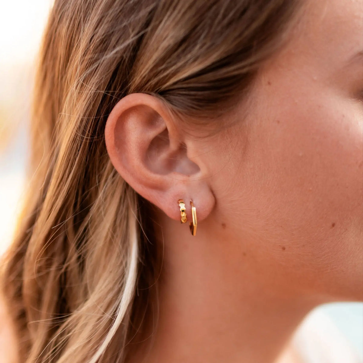 Close-up of a person wearing gold hoop earrings with blurred background