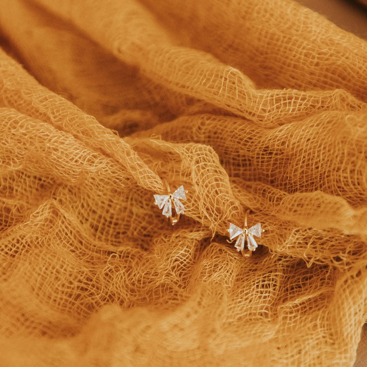 Pair of bow-shaped earrings on a textured brown fabric background