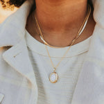 Close-up of a person wearing a gold necklace with an oval pendant.