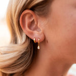 Close-up of a person wearing gold hoop earrings with a blurred background