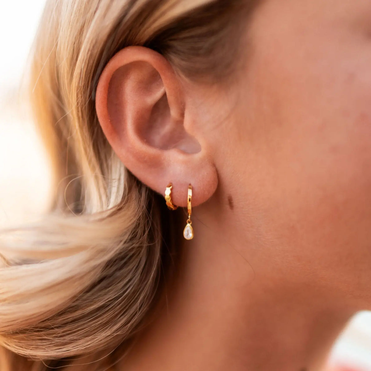 Close-up of a person wearing gold hoop earrings with a blurred background