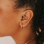 Close-up of an ear wearing gold hoop earrings with a bow detail.