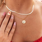 Gold necklace with a floral pendant worn by a person, with a hand touching the necklace.