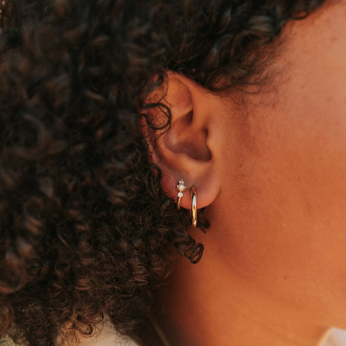 Close-up of an ear wearing gold hoop earrings with a blurred background