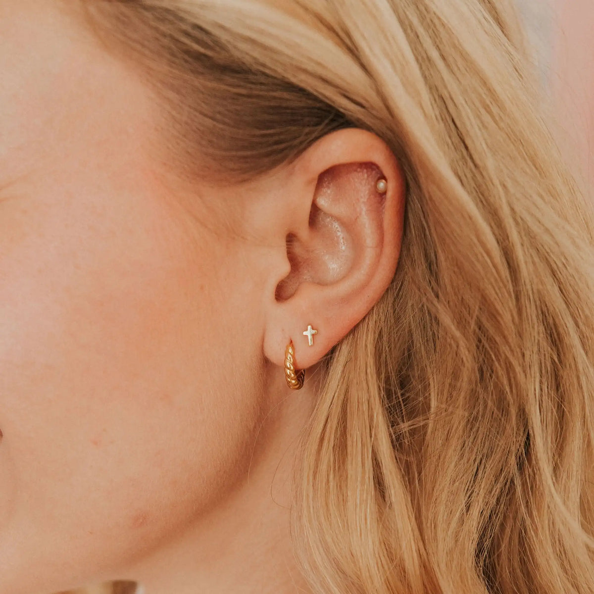 Close-up of an ear with gold hoop earrings and a cross stud.
