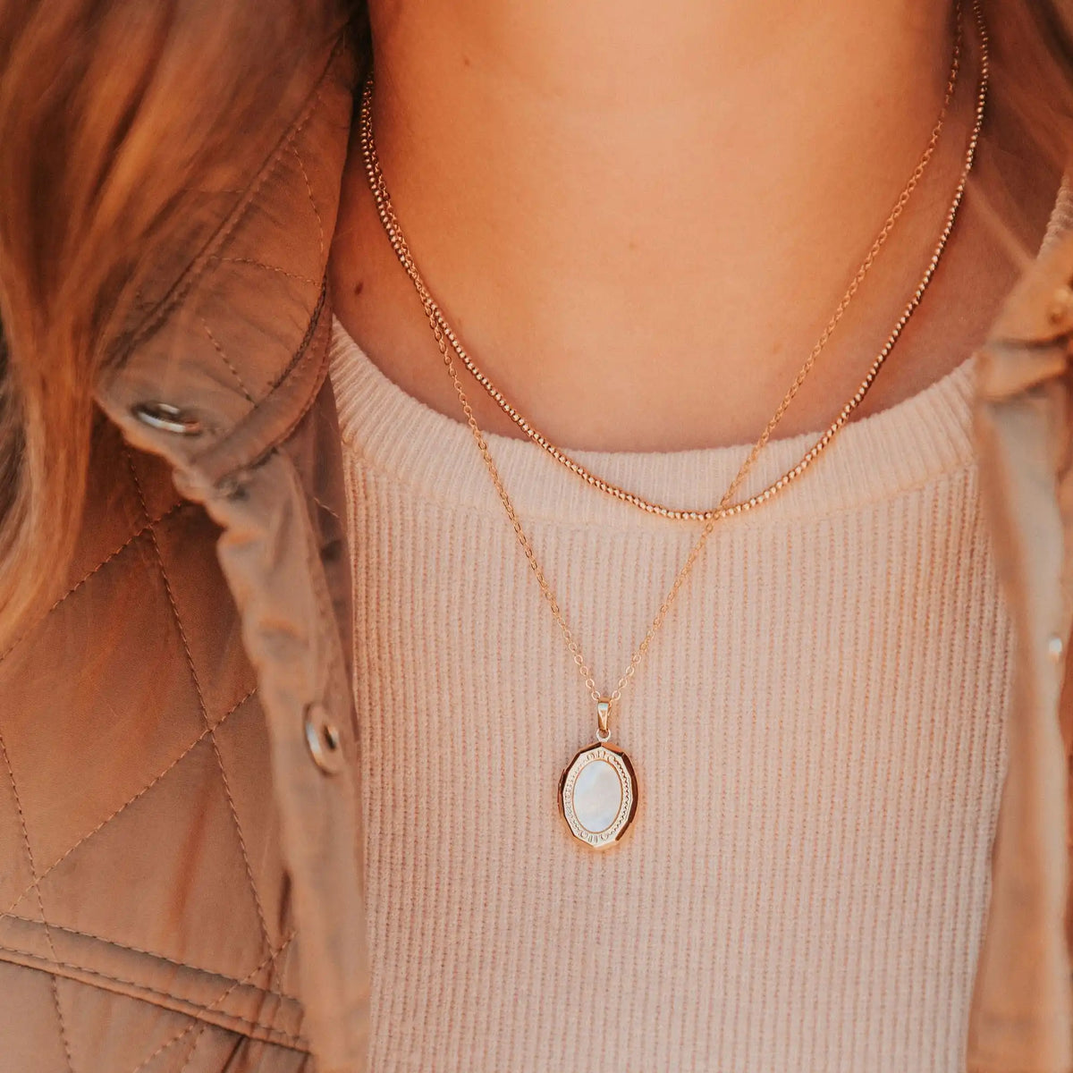 Close-up of a person wearing two gold necklaces with pendants.