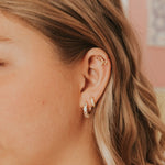 Close-up of an ear wearing gold earrings with a blurred background