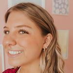 Close-up of a woman with styled hair and earrings against a pink wall.