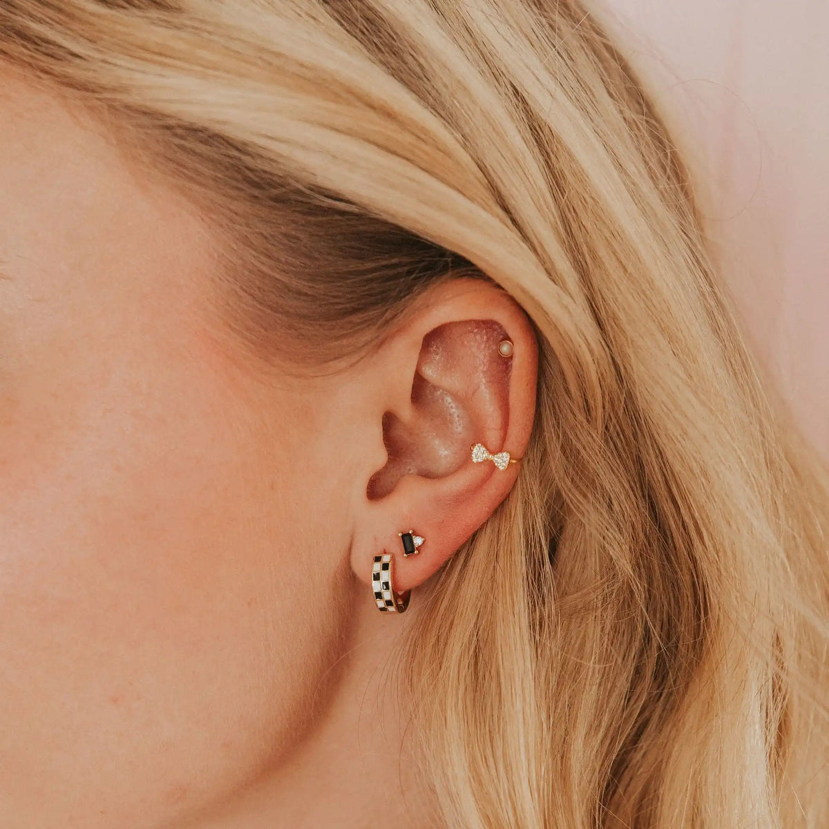 Close-up of a person's ear wearing two earrings with blonde hair.