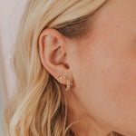 Close-up of a person wearing gold hoop earrings with a neutral background