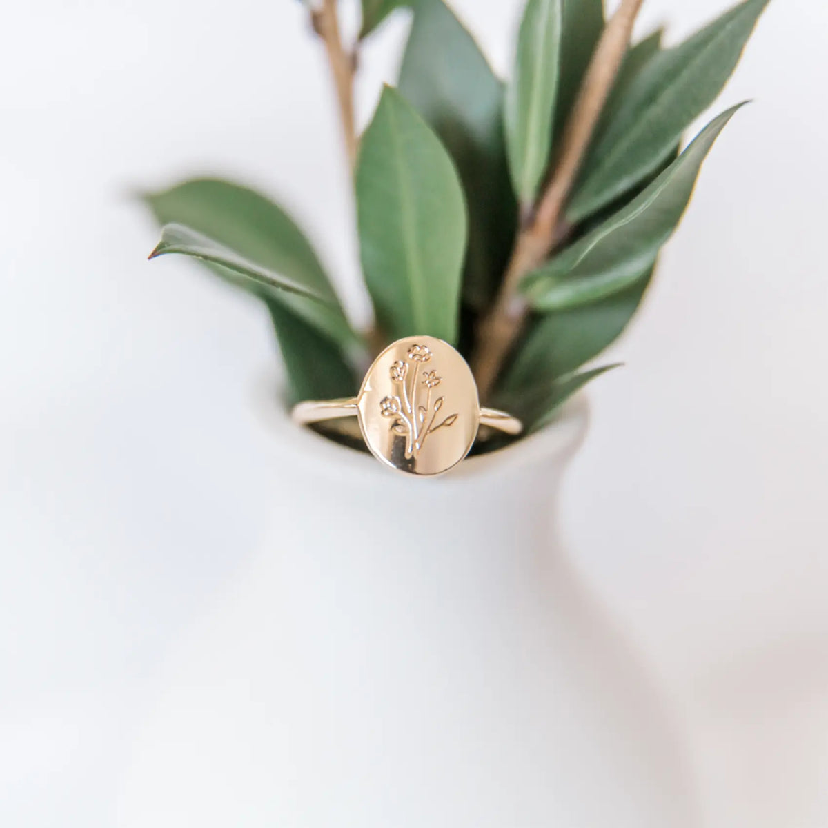 Gold ring with floral design on a white surface with green leaves