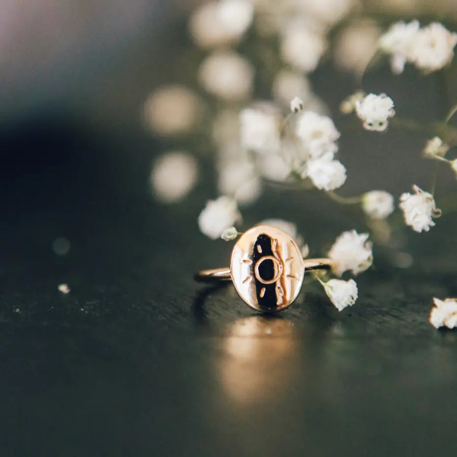 Gold ring with a black center on a dark surface with white flowers in the background