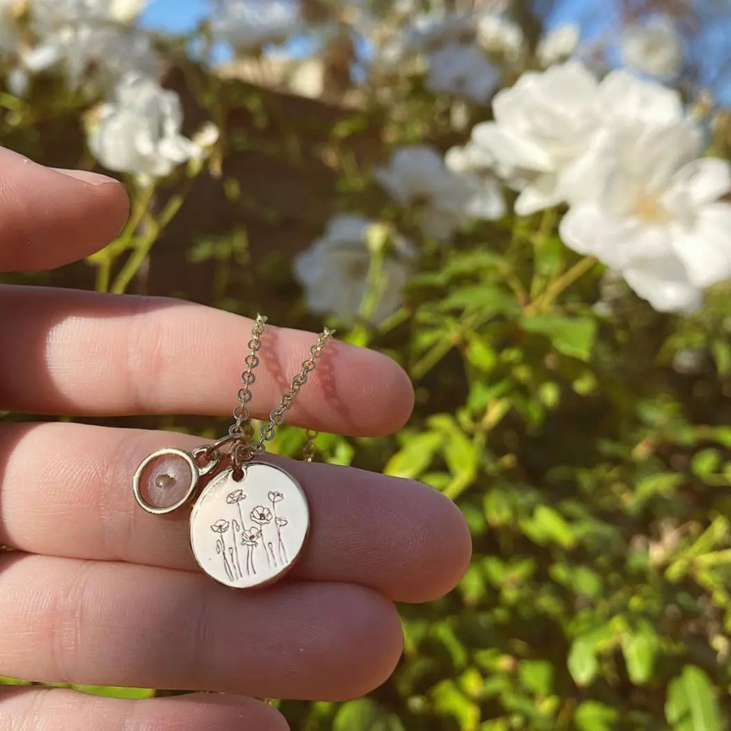 Gold necklace with a pendant held by a hand in front of white flowers