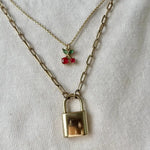 Gold necklace with a lock pendant and cherry charm on a white background