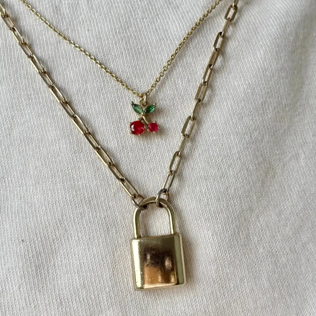 Gold necklace with a lock pendant and cherry charm on a white background