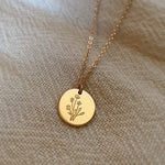 Gold necklace with a round pendant featuring an engraved design on a beige fabric background