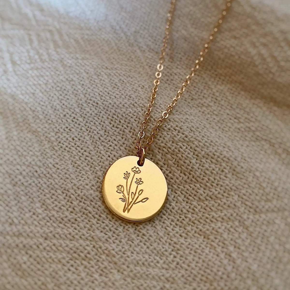 Gold necklace with a round pendant featuring an engraved design on a beige fabric background