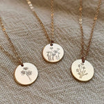 Three gold necklaces with circular pendants featuring floral designs on a textured fabric background.