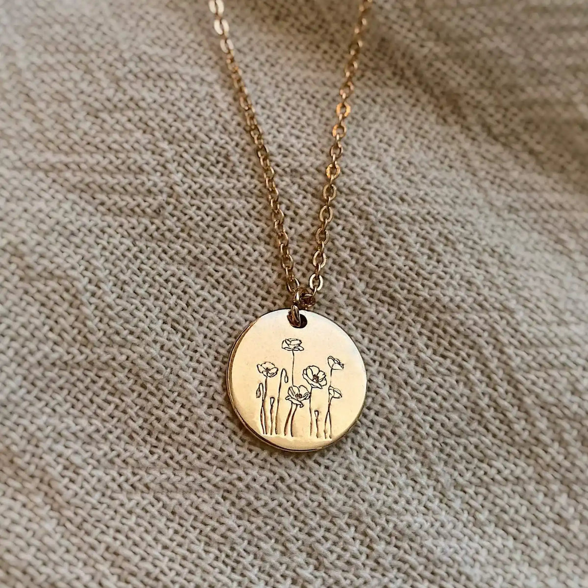 Gold necklace with a round pendant featuring floral designs on a textured beige fabric background
