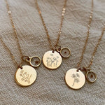 Load image into Gallery viewer, Three gold necklaces with engraved floral pendants on a textured fabric background
