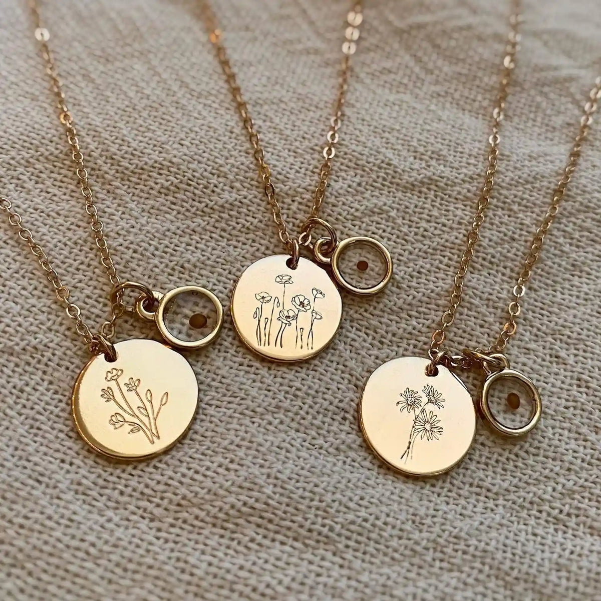 Three gold necklaces with floral pendants on a textured beige background