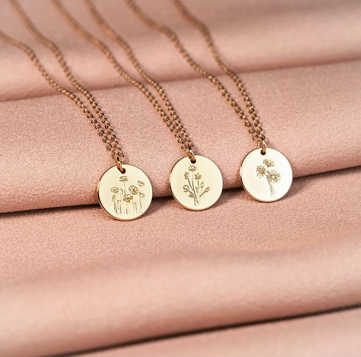 Three gold necklaces with engraved pendants on a pink fabric background