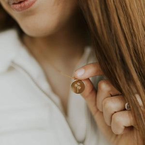 Close-up of a person holding a gold daisy floral necklace with a circular pendant.