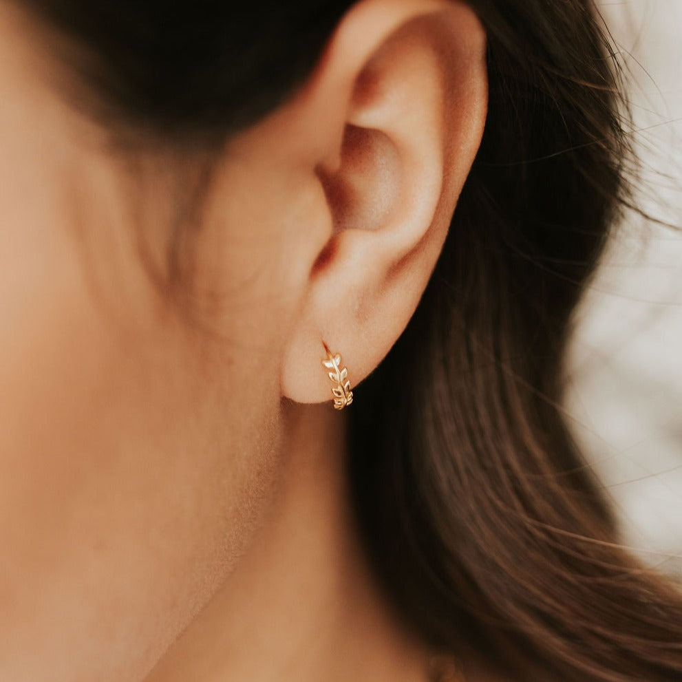 Woman wearing dainty gold hoop with intricate leafs on it. Tiny gold filled huggie earring over sterling silver.