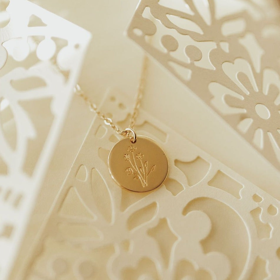 Gold necklace with a round pendant on a decorative white card