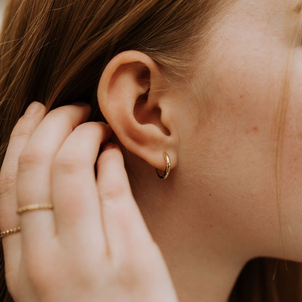 A close-up image of a woman's ear wearing a gold hoop earring.
