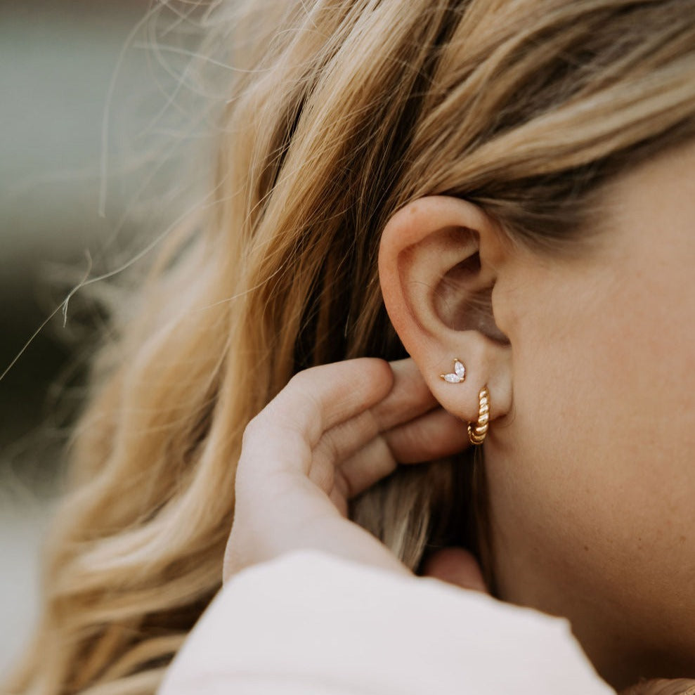 Close-up of a person wearing gold hoop earrings with a blurred background
